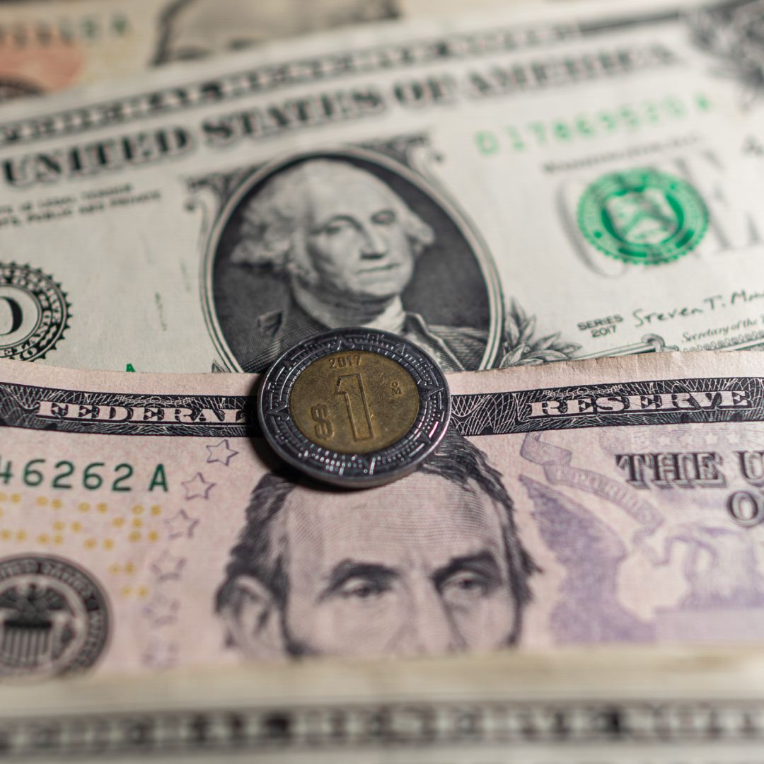Dólares junto a una moneda de un peso mexicano. Foto: N+